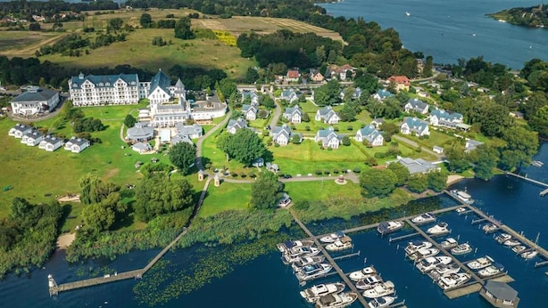An aerial view of a lakeside property with a large estate, smaller houses, and a marina with boats.