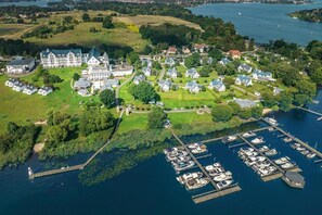 Vue aérienne d’une propriété au bord du lac, comprenant un grand domaine, des maisons plus petites et un port de plaisance avec des bateaux.