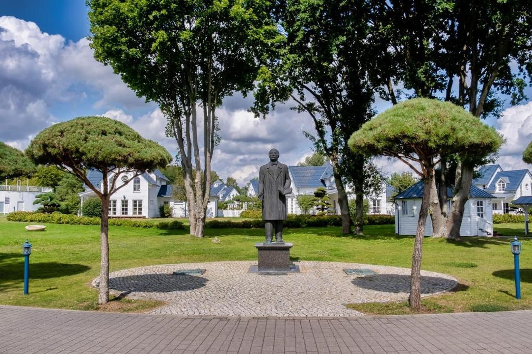 Una estatua en un parque con un sendero pavimentado, rodeada de árboles y casas.