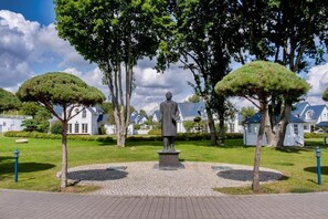 A statue in a park with a paved walkway, surrounded by trees and houses.