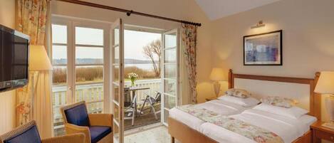 A bedroom with a bed, two chairs, a table with fruit, a TV, and a balcony with a view.