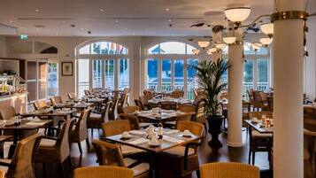 En restaurang med flera bord och stolar, stora fönster och en central pelare.