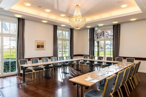 Une salle de conférence avec une longue table, des chaises, un lustre et de grandes fenêtres.