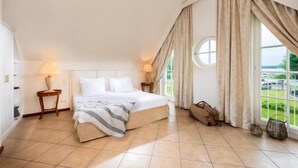 A bedroom with a large bed, two bedside tables, a window with curtains, and a view of the outside.