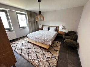 A modern bedroom with a large bed, a hanging light fixture, a nightstand, a chair, and a view of the outdoors. - Enjoy a cozy vacation in Loitz (Loitz)