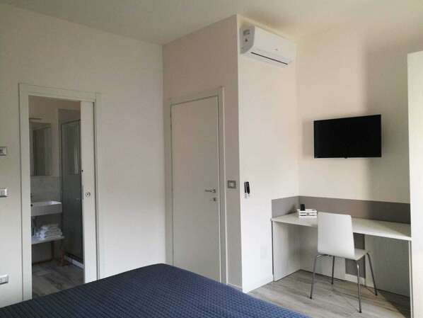 A bedroom with a bed, a desk, a chair, a TV, and an air conditioning unit.