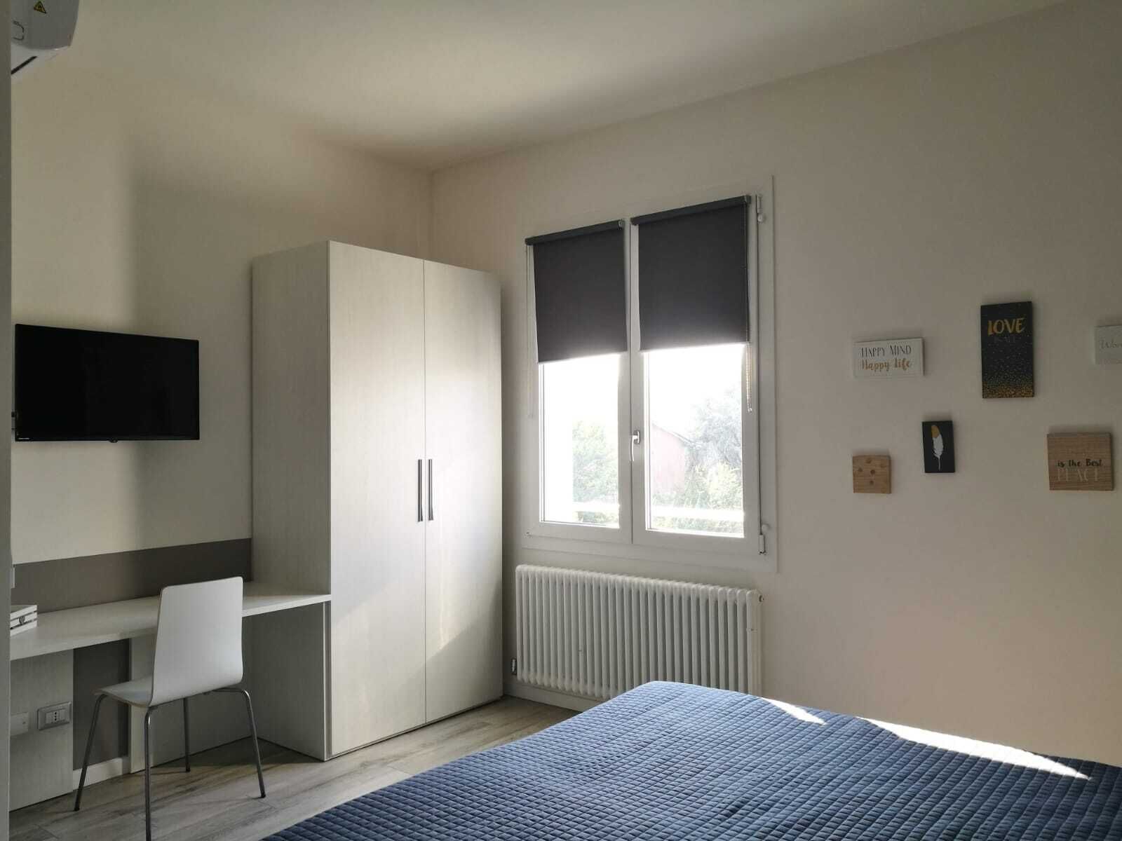 Une chambre à coucher comprenant un lit, un bureau, une chaise, une armoire, une fenêtre et des éléments décoratifs sur les murs.