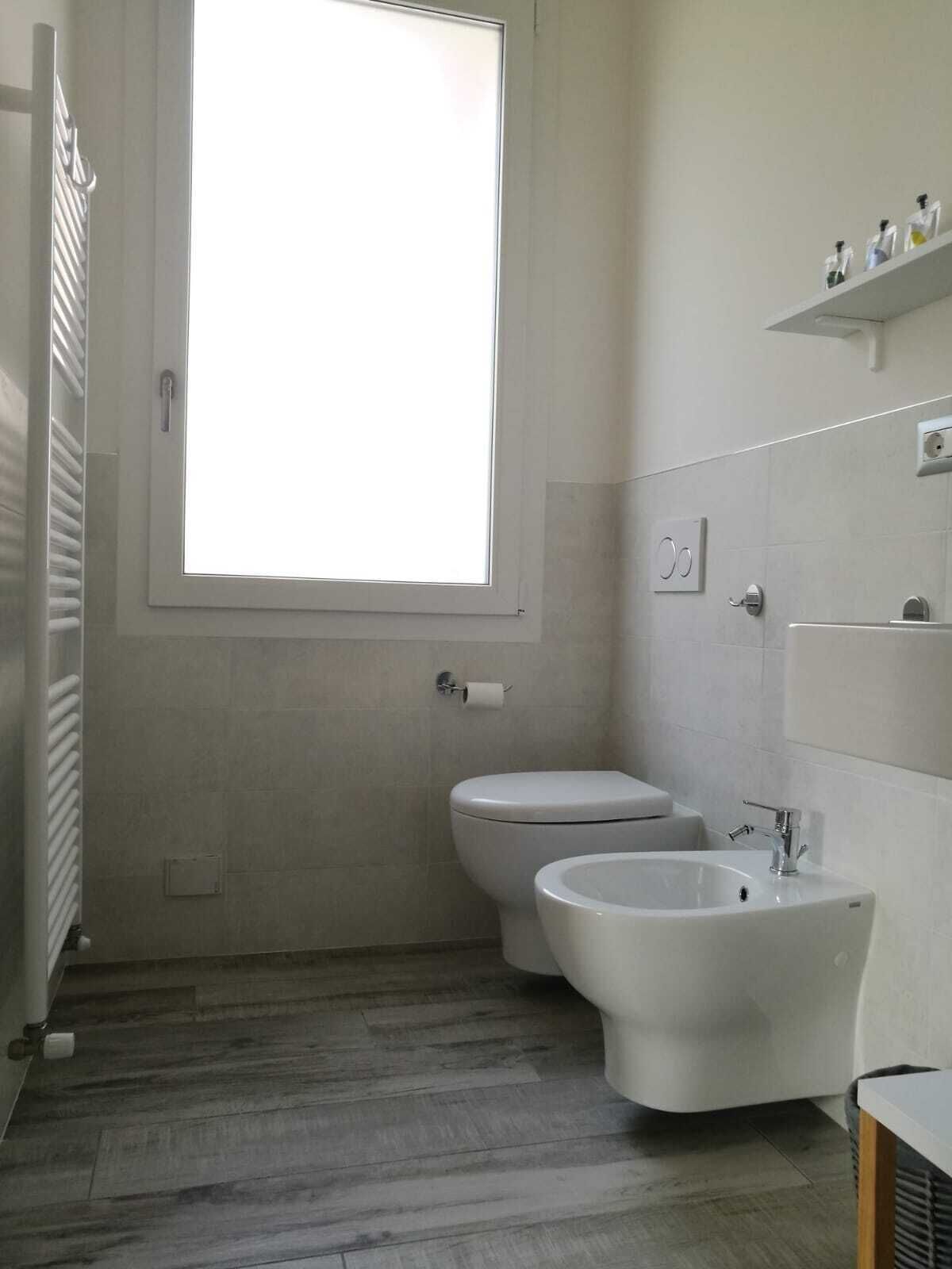 A bathroom with a toilet, bidet, and a window.