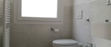 A bathroom with a toilet, bidet, and a window.
