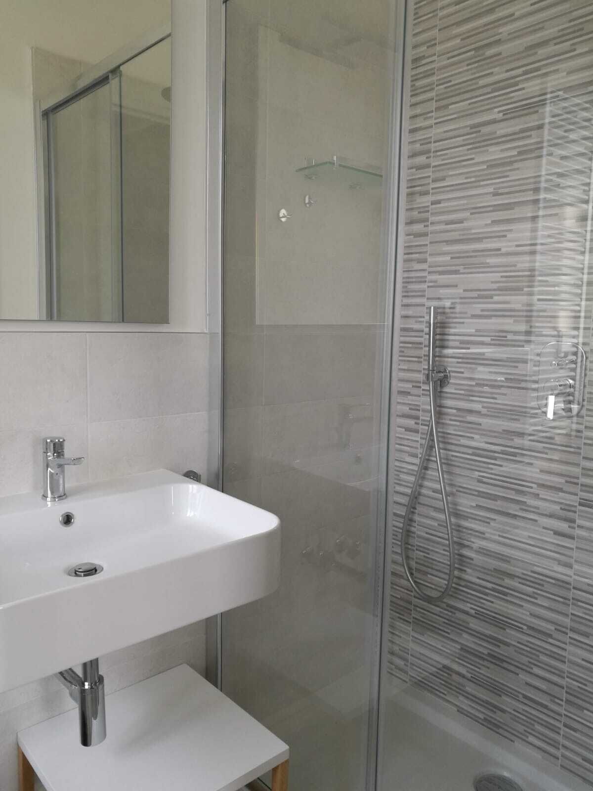 A modern bathroom with a white sink, a glass shower enclosure, and a mirror.