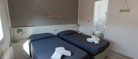 A hotel room with two beds, a bedside table with a lamp, a mirror, and a 'Dream' sign on the wall.