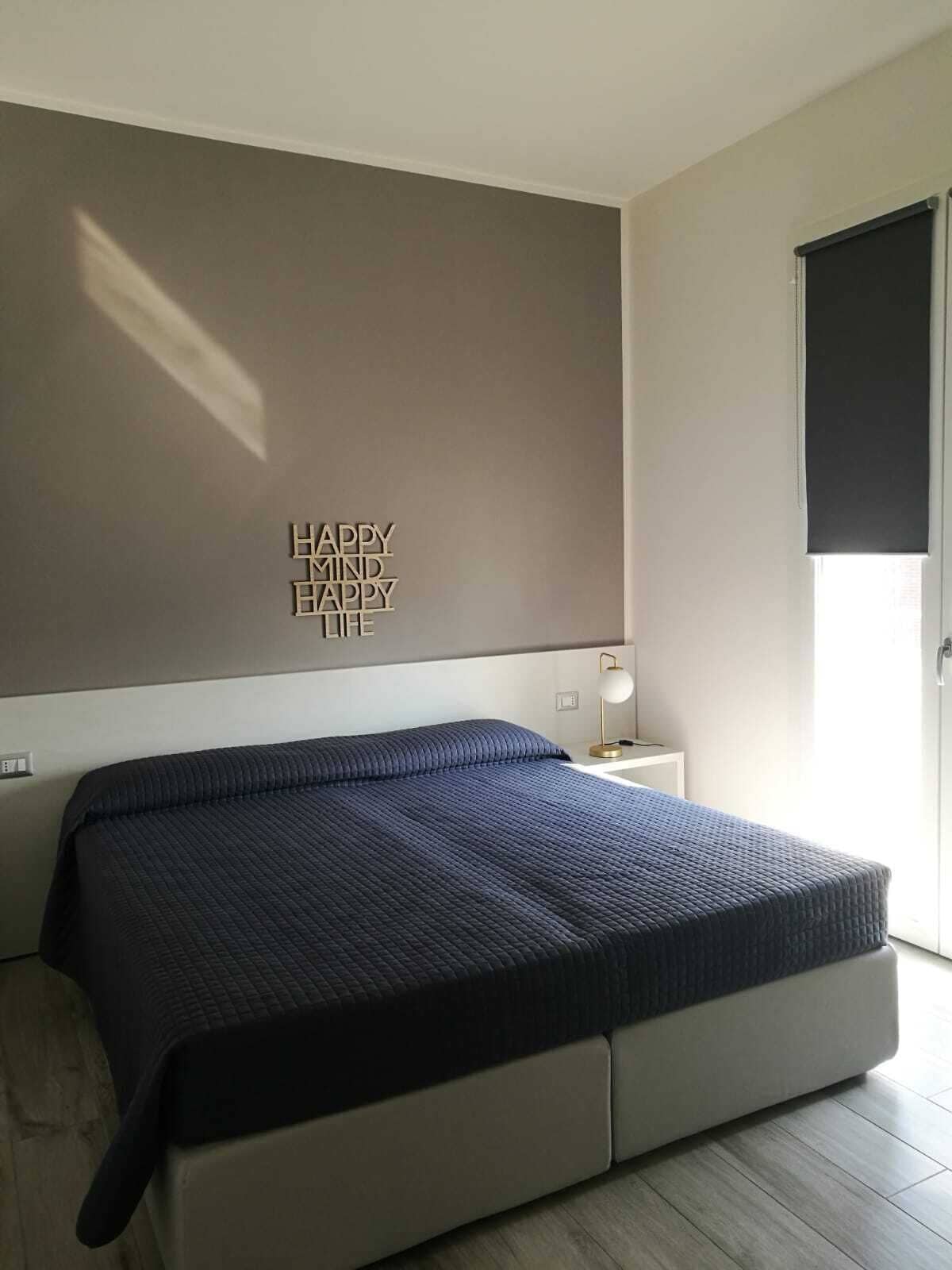 A modern bedroom with a bed, a wall-mounted light, and a motivational quote.