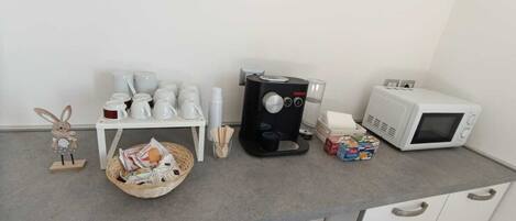 Una encimera de cocina con cafetera, microondas y varios utensilios.