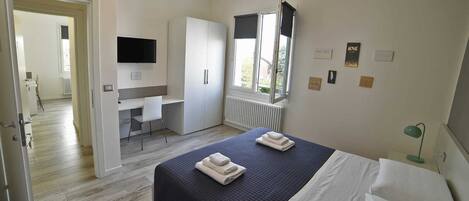 Un dormitorio con cama, escritorio, armario, televisor y ventana.