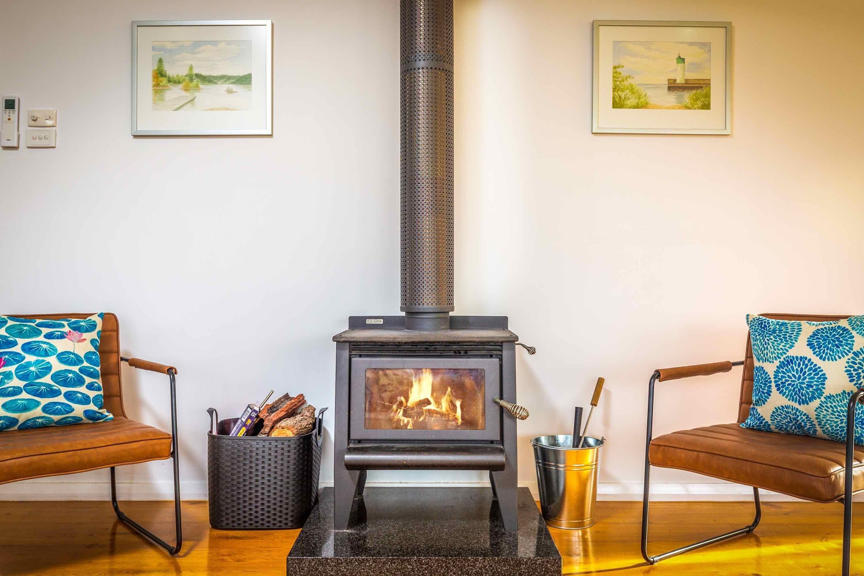 A room with a wood-burning stove, two chairs with patterned cushions, and framed artwork on the walls.
