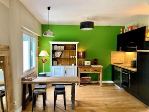 A kitchen with a green wall, wooden table, and black cabinets. - House with garden, 400m from the beach, all on foot, private parking (Wimereux)