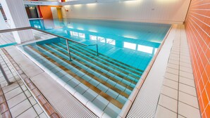 Una piscina interior con agua cristalina, escalones de cerámica para entrar y un techo de madera.