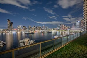 Une vue sur la ville, avec ses bâtiments modernes, son port de plaisance rempli de bateaux et un ciel nocturne dégagé.