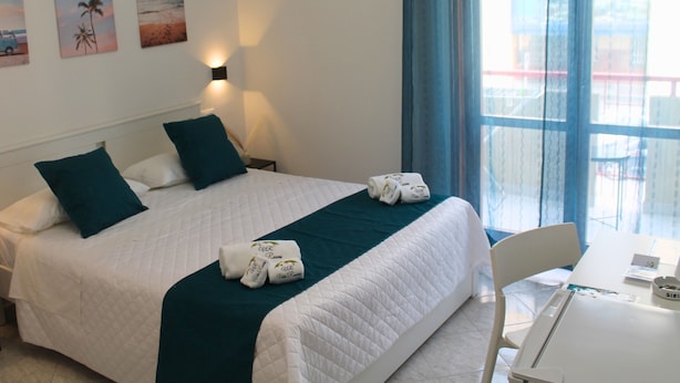 Une chambre d’hôtel avec un lit, deux oreillers, une table avec une chaise et une fenêtre avec des rideaux.