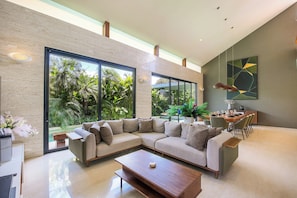 Un espacio de sala moderno con un sofá modular, una mesa de comedor y un amplio ventanal con vistas a un jardín exuberante.