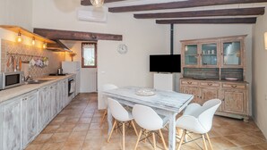 Una cocina con techo de madera, una mesa de comedor con sillas, un televisor y un mueble con puertas de vidrio.