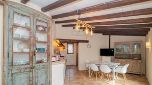 Una cocina rústica con vigas de madera a la vista, una zona de comedor con sillas blancas y un televisor montado en la pared.