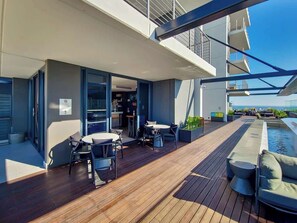 Una terrazza esterna moderna con pavimento in legno, zone relax e piscina.