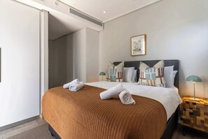 Una camera d'albergo con un letto, due abat-jour, un quadro appeso al muro e una porta che dà su un'altra stanza.