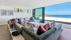 A modern living room with a large window overlooking a coastal view, a sofa set, and artwork on the walls. - Villa Rohalya: Sensational designer hideaway / 6BR (Cape Town)