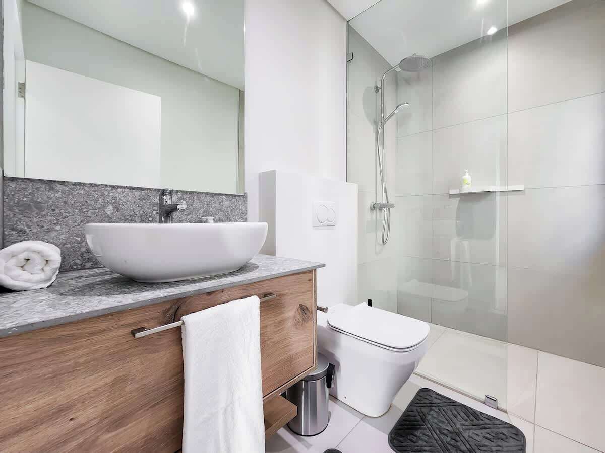 A modern bathroom with a large sink, a toilet, a glass shower enclosure, and a wooden vanity.