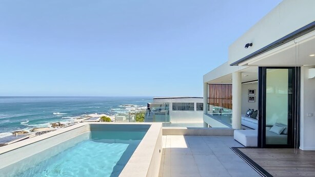 A modern pool with a clear view of the ocean, a glass-enclosed balcony, and a contemporary building structure. - Villa Rohalya: Sensational designer hideaway / 6BR (Cape Town)