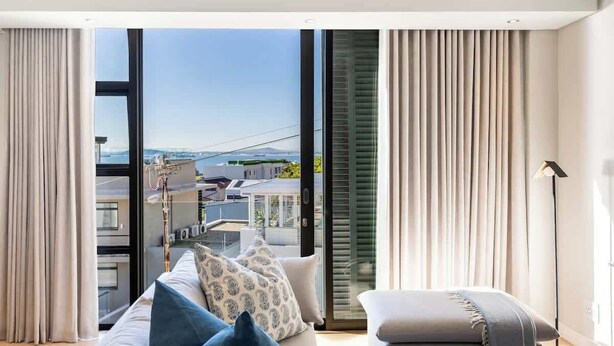 Een moderne woonkamer met een grote schuifpui, een bank met decoratieve kussens en een klein voetenbankje.