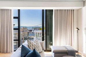 Un salon moderne doté d’une grande porte-fenêtre coulissante, d’un canapé avec des coussins à motifs et d’un petit pouf.