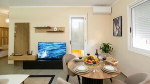 Una sala moderna con comedor, televisor de pantalla plana y mesa de comedor dispuesta con platos, vasos y fruta.