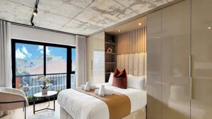 Ein modernes Hotelzimmer mit einem großen Bett, einem kleinen Tisch, einem Balkon mit Blick und eingebauten Schränken.