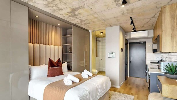 Ein modernes Hotelzimmer mit einem großen Bett, einer integrierten Garderobe und einer Küchenzeile.