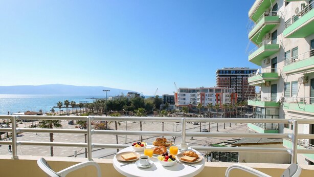 A balcony with a table set for breakfast, overlooking a beach and cityscape. - Luna Sea View Apartment 5 Floor (Vlorë)