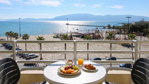 A balcony with a table set for breakfast overlooking a beach and the sea. - Luna Sea View Apartment 5 Floor (Vlorë)