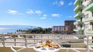A balcony with a table set for breakfast overlooking a beach and cityscape. - Luna Sea View Apartment 5 Floor (Vlorë)