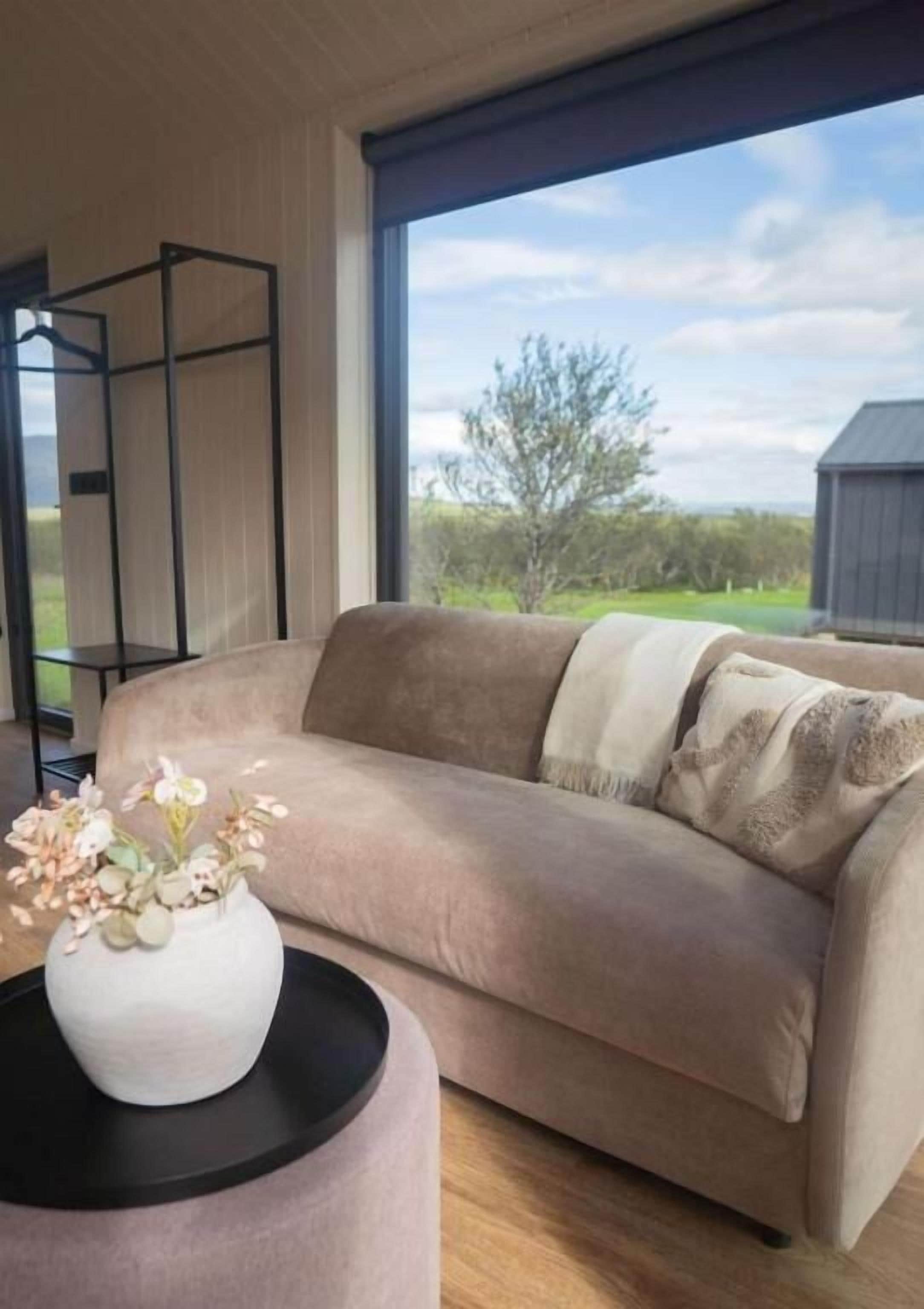 A beige sofa with a throw blanket, a white vase with flowers, and a black side table.