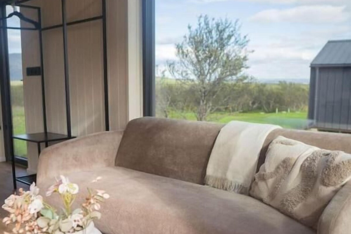 A beige sofa with a throw blanket, a white vase with flowers, and a black side table.