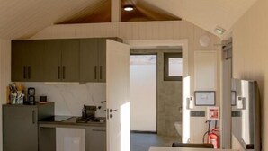 A compact room with a bed, a dining table, a kitchenette, and a small bathroom. - Golden Circle Cabins (Laugarvatn)