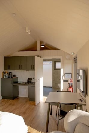 A compact room with a bed, a dining table, a kitchenette, and a small bathroom. - Golden Circle Cabins (Laugarvatn)