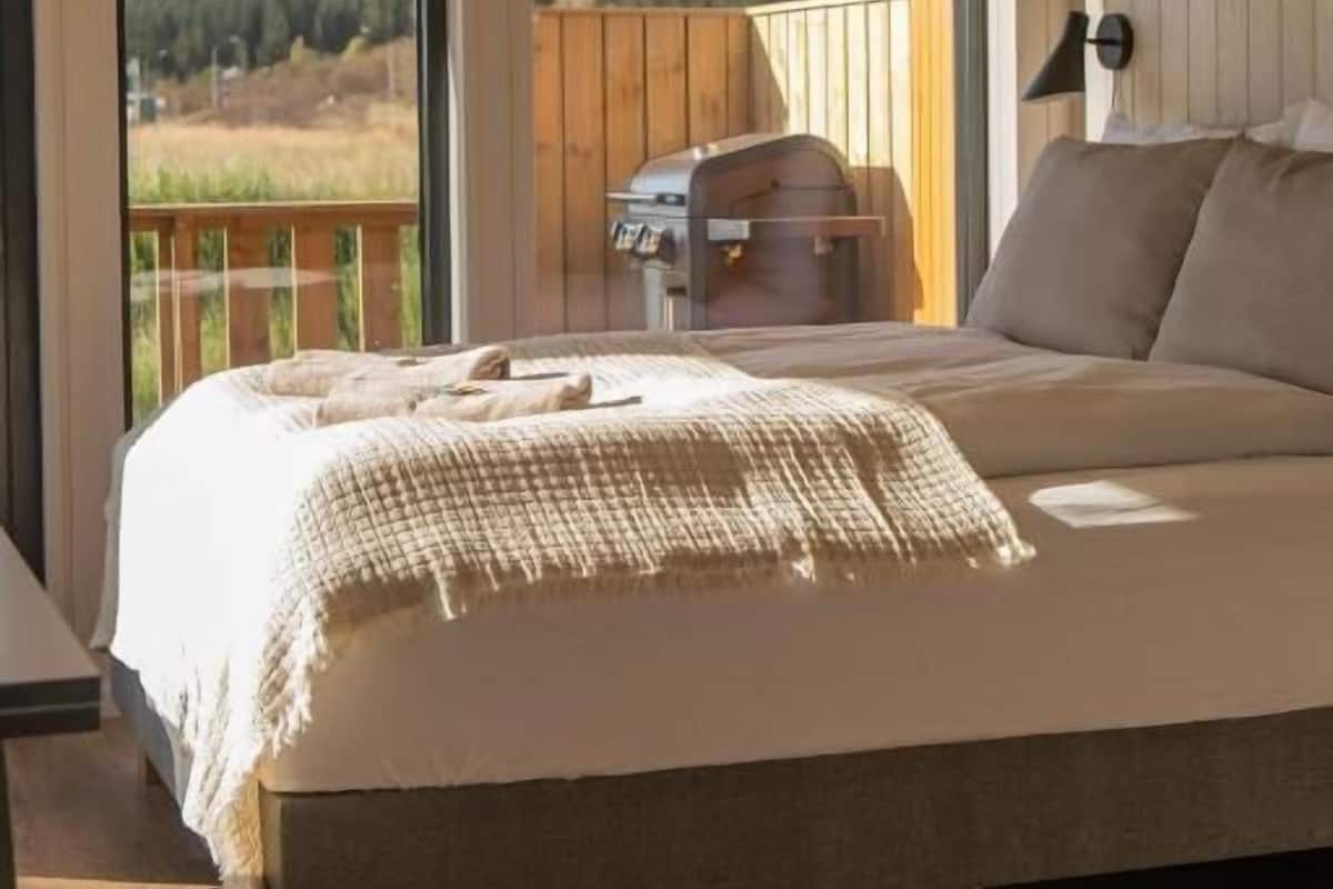 A bedroom with a large bed, wooden walls, and a view of a forest.