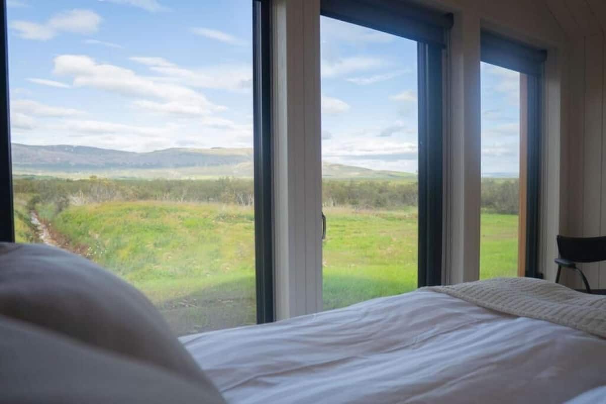 A bedroom with a large window overlooking a grassy landscape.