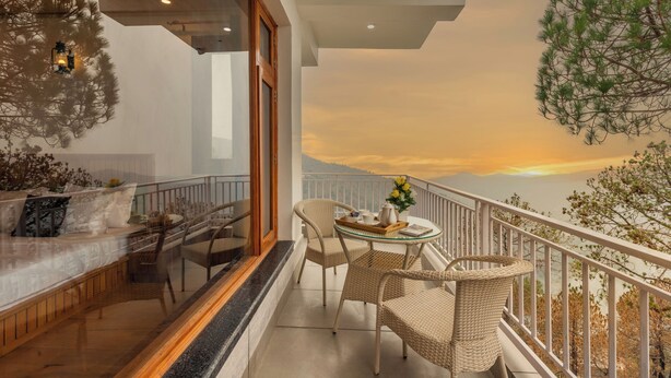 A balcony with wicker furniture, a glass table, and a view of the sunset. - Alaya Stays Querencia 5BHK with HillView (Kasauli)
