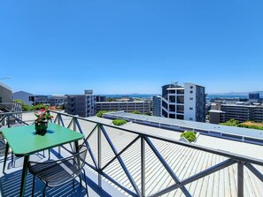 En tagterrasse med et bord og stole, udsigt over bybilledet og en klar blå himmel.