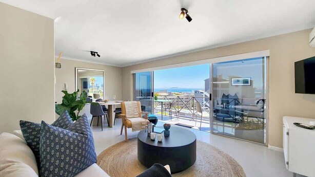 A modern living room with a sofa, coffee table, and a dining area with chairs. - Casa del Mar: Sparkling secure 2BR, Wi-Fi, parking (Cape Town)