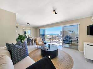 A modern living room with a sofa, coffee table, and a dining area with chairs. - Casa del Mar: Sparkling secure 2BR, Wi-Fi, parking (Cape Town)