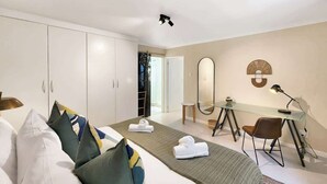 A hotel room with a bed, a desk, a chair, a mirror, and a wardrobe. - Casa del Mar: Sparkling secure 2BR, Wi-Fi, parking (Cape Town)